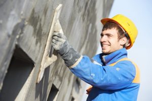 builder worker plastering facade industrial building with putty knife float